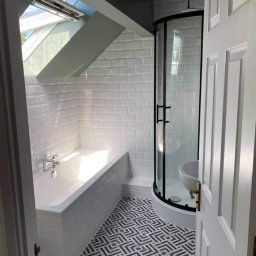 racsobuild - Wykończona łazienka na poddaszu z oknem dachowym, białe płytki typu metro na ścianach, kabina prysznicowa z czarną obudową, wanna obudowana płytkami, czarno-biała podłoga w geometryczny wzór.