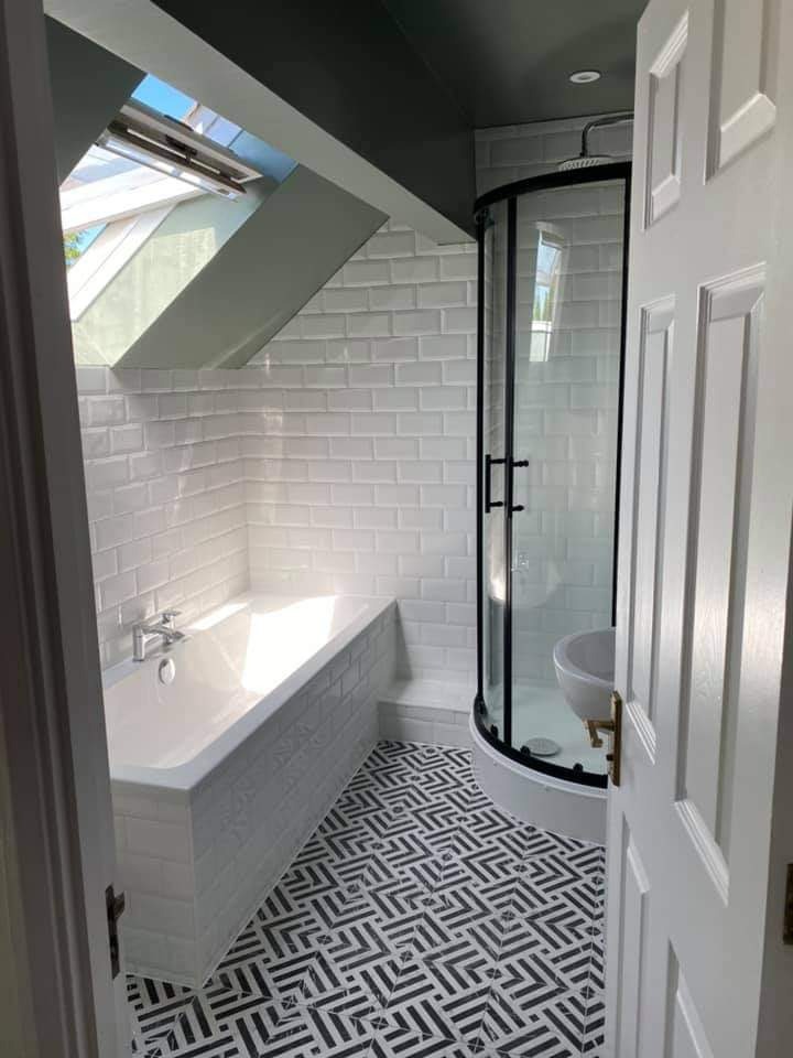 Wykończona łazienka na poddaszu z oknem dachowym, białe płytki typu metro na ścianach, kabina prysznicowa z czarną obudową, wanna obudowana płytkami, czarno-biała podłoga w geometryczny wzór.