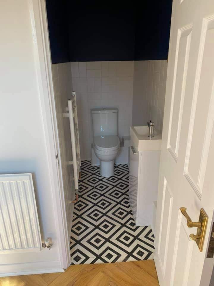 Wnętrze wyremontowanej łazienki z białą armaturą, czarno-białą geometryczną podłogą i ciemnoniebieskim sufitem, widoczne zza otwartych białych drzwi.