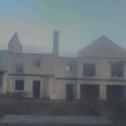 Surowy stan budynku w Dusznikach, widoczne ściany z pustaków, otwory okienne i kominy w trakcie budowy, teren wokół przygotowany pod dalsze prace.