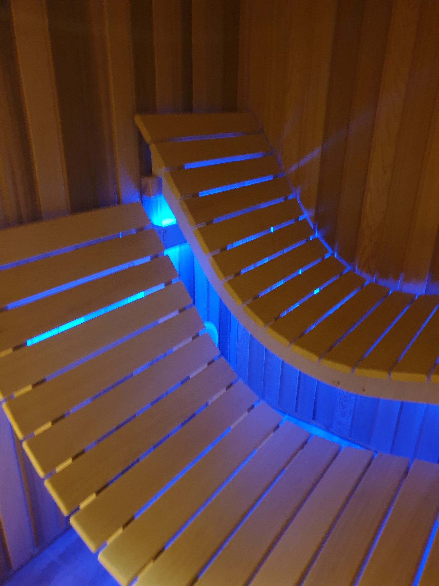 Wnętrze sauny z drewnianymi, profilowanymi ławkami podświetlonymi niebieskim światłem LED.