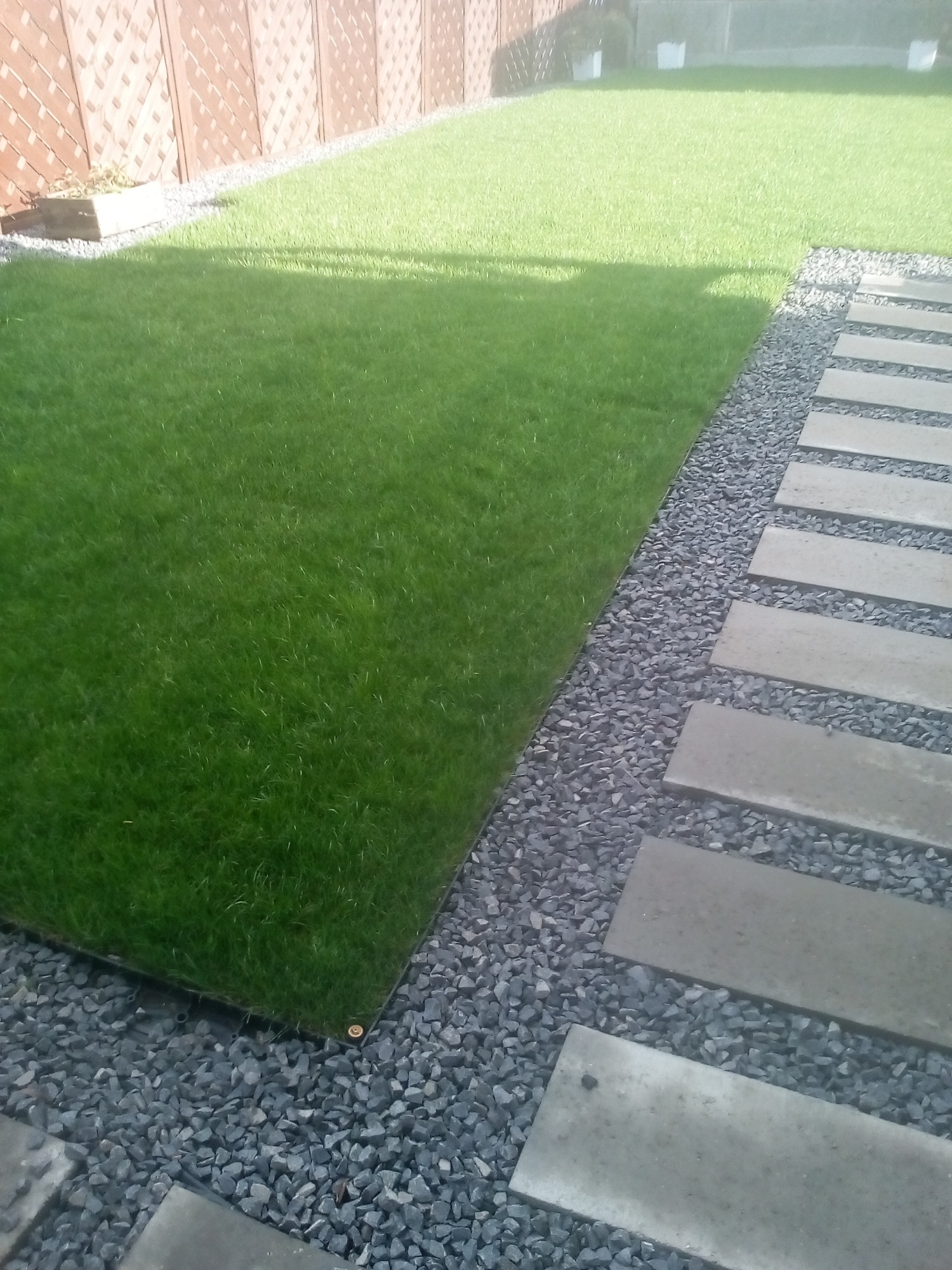 Fragment trawnika z syntetycznej trawy, obrzeże z szarego grysu i ścieżka z płyt betonowych w ogrodzie.
