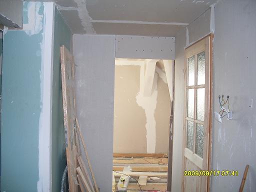 Wnętrze w trakcie remontu: widoczne płyty gipsowo-kartonowe na ścianach i suficie, drewniane elementy konstrukcyjne, surowe wykończenie, otwarta przestrzeń z widocznymi elementami instalacji...