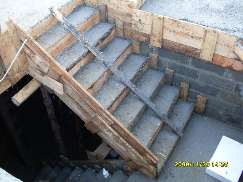Betonowe schody w trakcie budowy, z drewnianym szalunkiem, widoczne bloczki fundamentowe i data na zdjęciu.