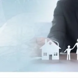 Mężczyzna w garniturze gestykuluje dłońmi nad papierowymi wycinankami przedstawiającymi dom, rodzinę i samochód na tle abstrakcyjnej grafiki.