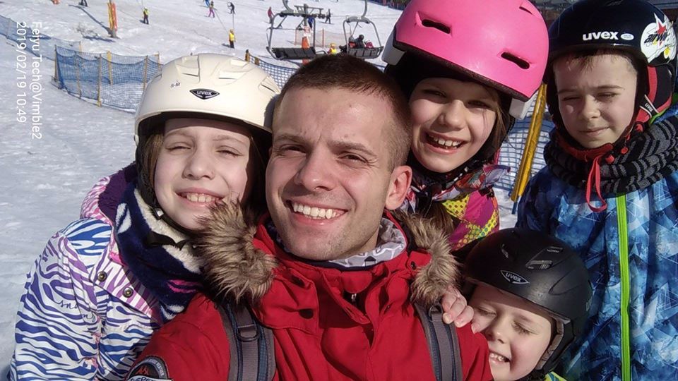 Instruktor sportów walki z Gdańska pozuje do selfie z grupą dzieci na stoku narciarskim, widoczne wyciągi krzesełkowe w tle.