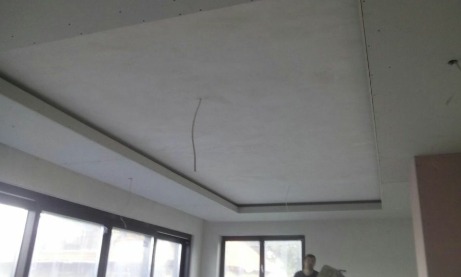 Wykończony sufit podwieszany z płyt kartonowo-gipsowych, widoczne łączenia i wystające kable, przygotowany do dalszych prac wykończeniowych, takich jak szpachlowanie i malowanie, z oknami w tle.