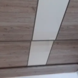 Fragment szafy z przesuwnymi drzwiami, z frontami w kolorze drewna i białym pasem pośrodku, widoczne z dołu pod kątem.