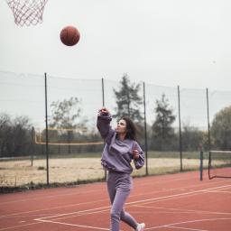 Marika Małek - Kobieta w liliowym dresie marki Claire rzuca piłkę do kosza na czerwonym boisku sportowym.