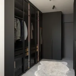 Czarna garderoba z podświetlanymi pionowymi paskami, ubrania wewnątrz, puszysty biały dywan na szarym betonowym podłożu, minimalistyczne oświetlenie punktowe.