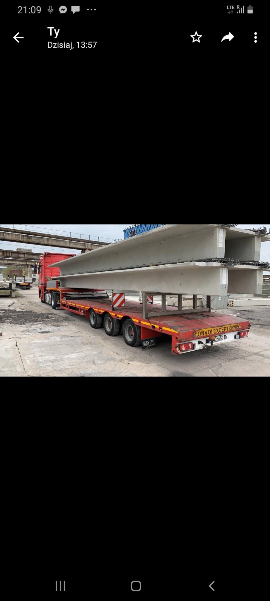 Czerwona ciężarówka transportuje dwa betonowe elementy konstrukcyjne na niskopodwoziowej platformie z napisem 'CONVOI EXCEPTIONNEL'.