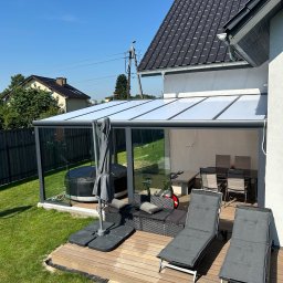 Elkano - Zadaszony taras z drewnianą podłogą, wyposażony w jacuzzi, leżaki i stół z krzesłami. Widok na ogród i dom w tle, słoneczny dzień.