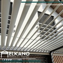 Elkano - Nowoczesna pergola z jasnymi lamelami, widok z dołu, z logo firmy ELKANO. Minimalistyczny design, gra światła i cienia na białej fasadzie budynku.