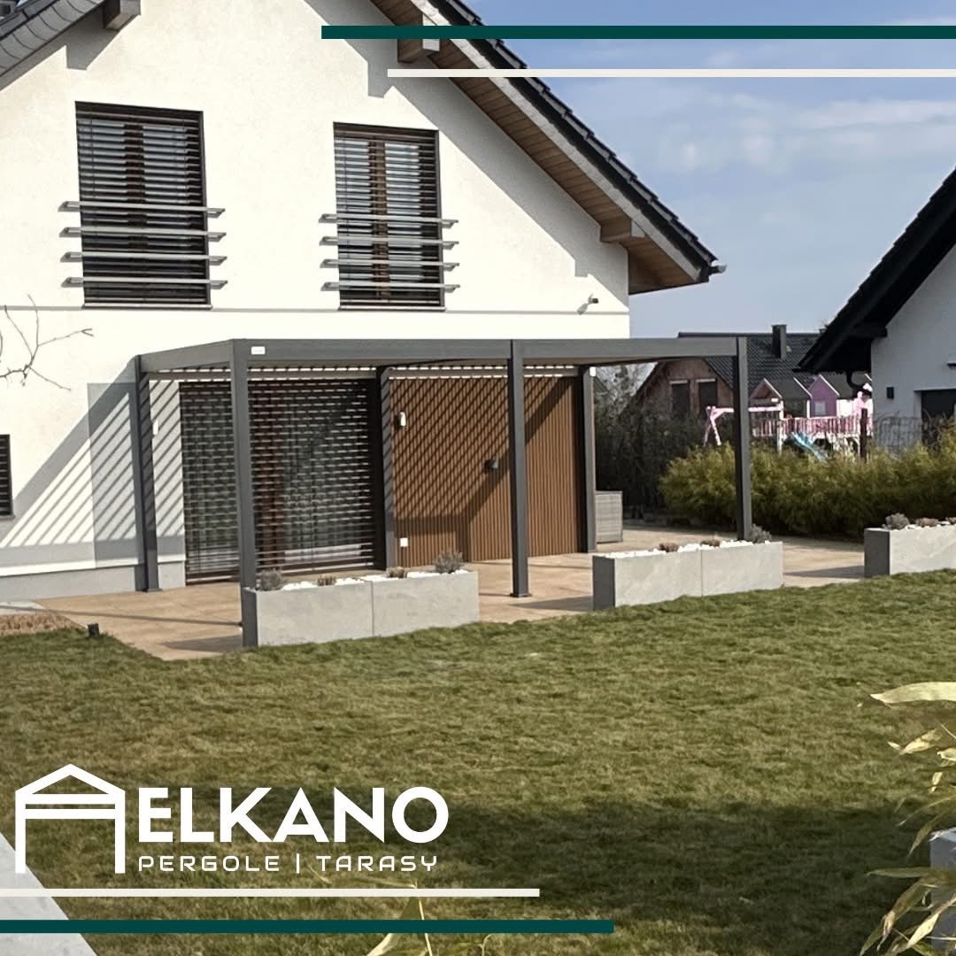 Nowoczesna pergola z szarym stelażem i drewnianym panelem, zintegrowana z domem. Betonowe donice z roślinami na tarasie i trawnik przed domem.