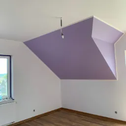 Pokój na poddaszu po remoncie: białe ściany, drewniana podłoga, fioletowy fragment sufitu, widoczne okno i grzejnik.