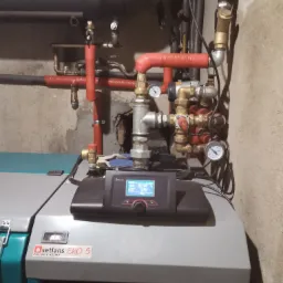 Kocioł na paliwo stałe Setlans EKO 5 z podłączoną instalacją, widoczne rury w izolacji termicznej, manometry i sterownik Plum z wyświetlaną temperaturą.