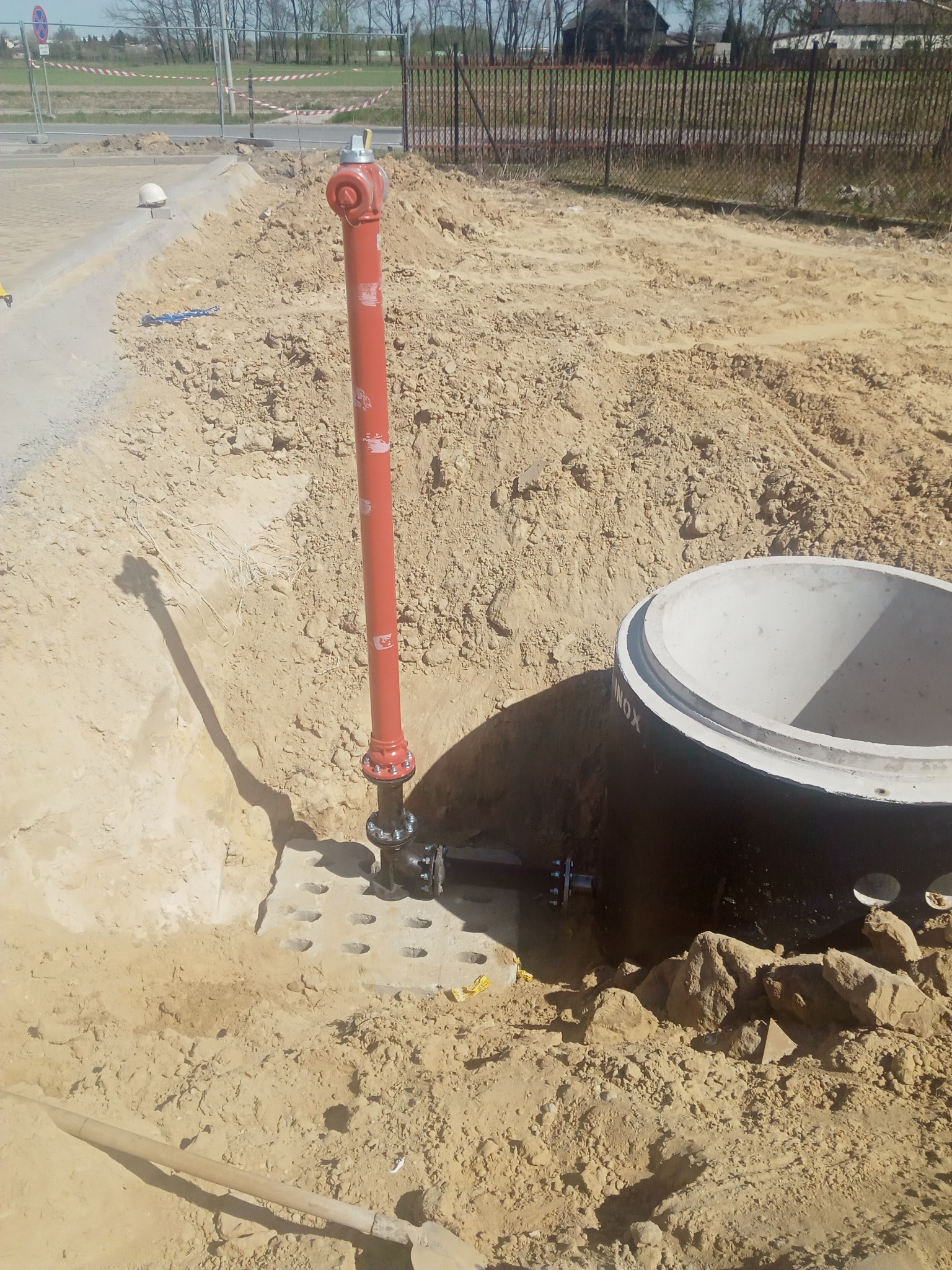 Montaż hydrantu przeciwpożarowego i betonowego kręgu studni w Poradzewie, widoczne wykopy i narzędzia.