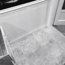 Fragment pomieszczenia z wykończonymi ścianami w panelach i szarą podłogą, widoczny fragment szafki z metalowym wykończeniem i dekoracja ściany z rybą.