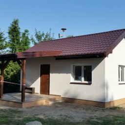 F.R.B. INBUD Robert Lipowski - Nowo otynkowany budynek gospodarczy z brązowym dachem i drewnianą werandą, otoczony zielenią i zabezpieczony taśmą ostrzegawczą.