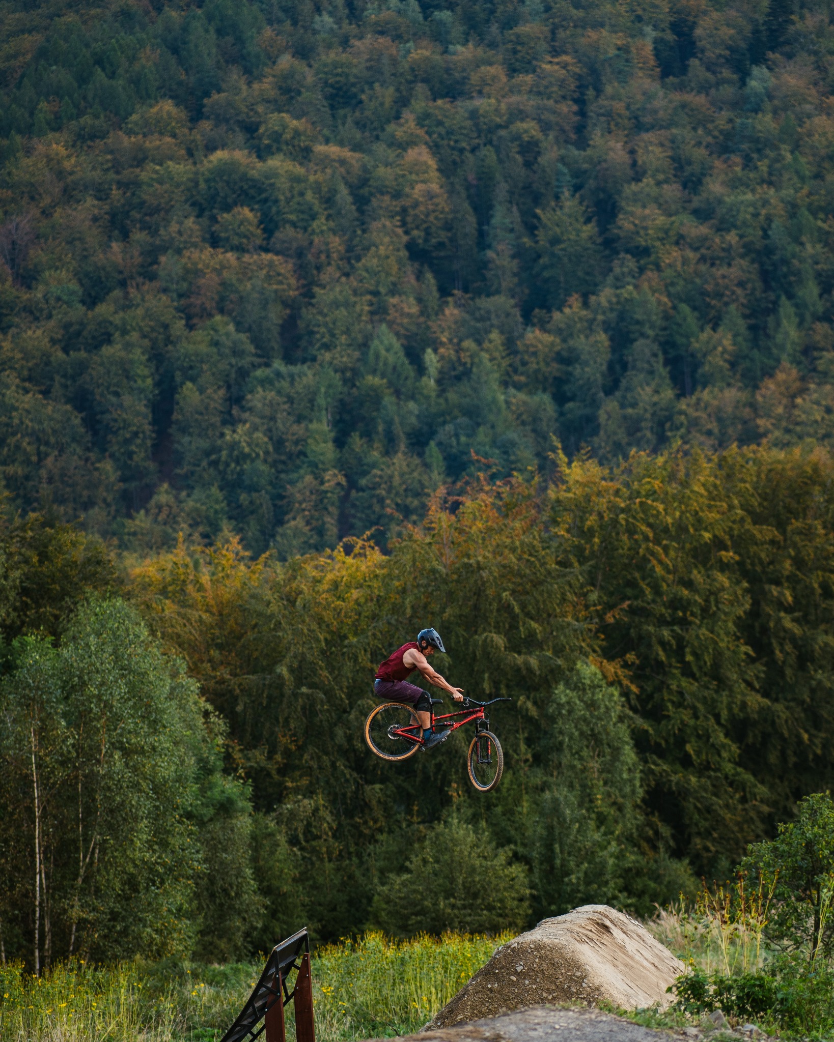 Rowerzysta w kasku wykonuje skok na rowerze górskim z rampy, w tle las w okolicach Warszawy.