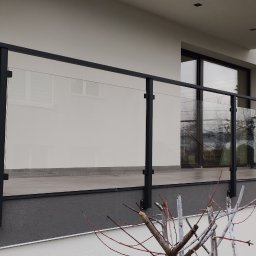 Alu Prospect - Nowoczesna balustrada szklana z czarnymi profilami na balkonie domu jednorodzinnego. Widok na elewację z oknami. Minimalistyczny design, jasna kolorystyka.