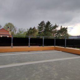 Alu Prospect - Nowoczesna balustrada szklana z grafitowymi słupkami na tarasie, z widokiem na drzewa i pochmurne niebo w tle. Minimalistyczny design i funkcjonalność.