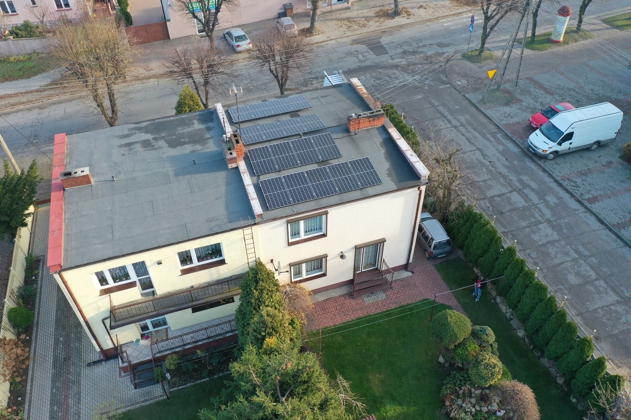 Widok z góry na dom w Klonowej z panelami słonecznymi na dachu, drabina oparta o ścianę, zadbany ogród i zaparkowane samochody w pobliżu.