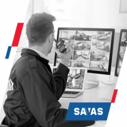 Pracownik ochrony w mundurze, z krótkofalówką w dłoni, monitoruje ekrany z podglądem z kamer w pomieszczeniach.