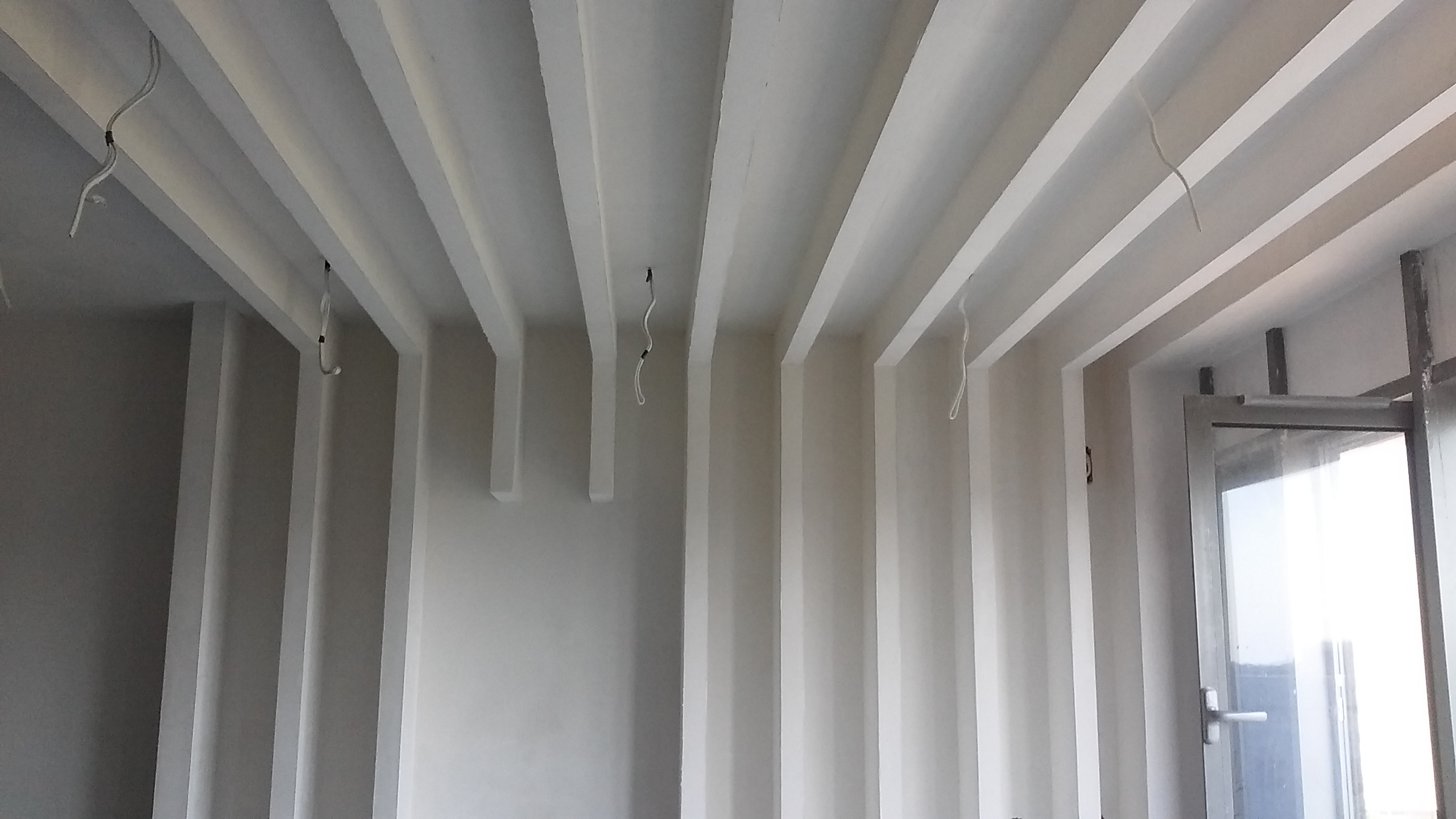 Wykończone wnętrze z dekoracyjnymi, pionowymi i poziomymi elementami na ścianach i suficie, świeżo po malowaniu, z widocznymi przewodami elektrycznymi.