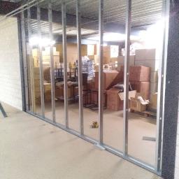 Krystian Napiorkowski - Montaż metalowej konstrukcji ścianki działowej w magazynie, widoczne kartony i narzędzia pracy.