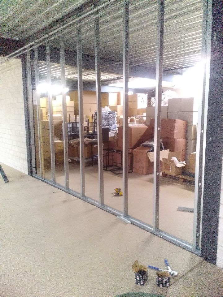 Montaż metalowej konstrukcji ścianki działowej w magazynie, widoczne kartony i narzędzia pracy.