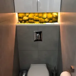 Nowoczesna łazienka z szarą glazurą, podwieszaną toaletą i dekoracyjną ścianą z mchu podświetloną ledami, umieszczoną nad spłuczką.