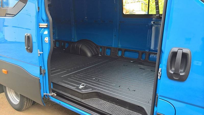 Wnętrze niebieskiego busa po zabezpieczeniu antykorozyjnym, widoczna nowa, czarna, żebrowana podłoga ładunkowa i zabezpieczone profile. Otwarta boczna ściana z uchwytem.