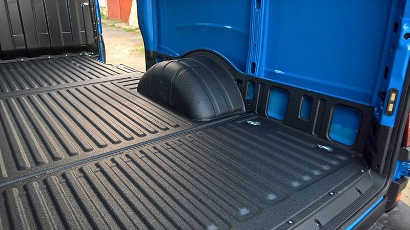 Wnętrze paki dostawczego samochodu z zabezpieczoną, czarną, ryflowaną powierzchnią podłogi i nadkoli, błękitne ściany boczne, uchwyty mocujące ładunek.