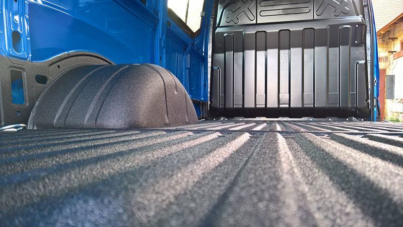 Wnętrze paki dostawczego samochodu po nałożeniu ochronnej, chropowatej powłoki w kolorze grafitowym, widoczne elementy karoserii w kolorze niebieskim.