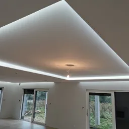 Nowoczesne wnętrze z podwieszanym sufitem oświetlonym ledami, widoczne duże okna przesuwne i surowa podłoga.