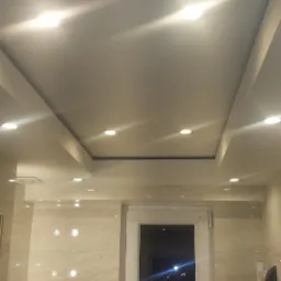 Podwieszany sufit w łazience z oświetleniem punktowym, widoczne płytki na ścianach i okno.