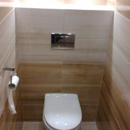 Kamil Rogalski - Nowoczesna toaleta w beżowych odcieniach, z podświetleniem LED nad płytkami z motywem kwiatowym i chromowanym przyciskiem spłukującym.