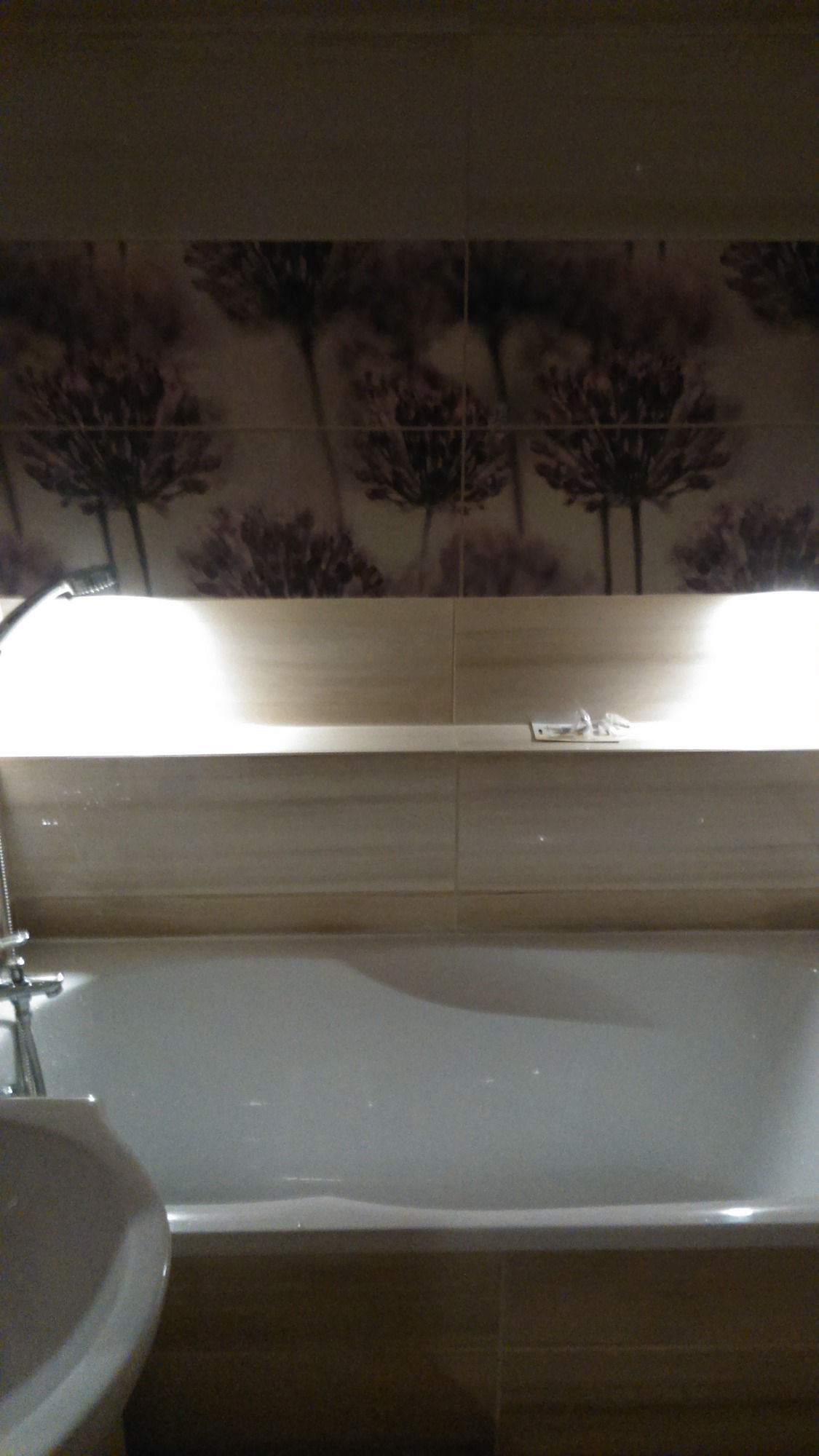 Wykończona łazienka w Wyszkowie: wanna obudowana płytkami w odcieniach beżu, nad nią dekoracyjne płytki z motywem kwiatowym w tonacji fioletowo-brązowej, chromowana bateria.