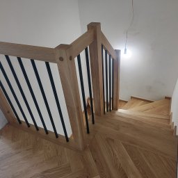 P.P.H.U. JAROSŁAW SMAGA - Drewniane schody z czarnymi, metalowymi balustradami, widok z góry. Parkiet ułożony w jodełkę. Surowe wykończenie ścian i wisząca żarówka.