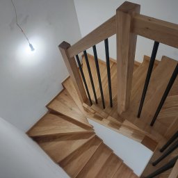 P.P.H.U. JAROSŁAW SMAGA - Drewniane schody z czarnymi balustradami, widok z góry. Naturalne drewno, minimalistyczny design. W tle surowa ściana z wiszącą żarówką.