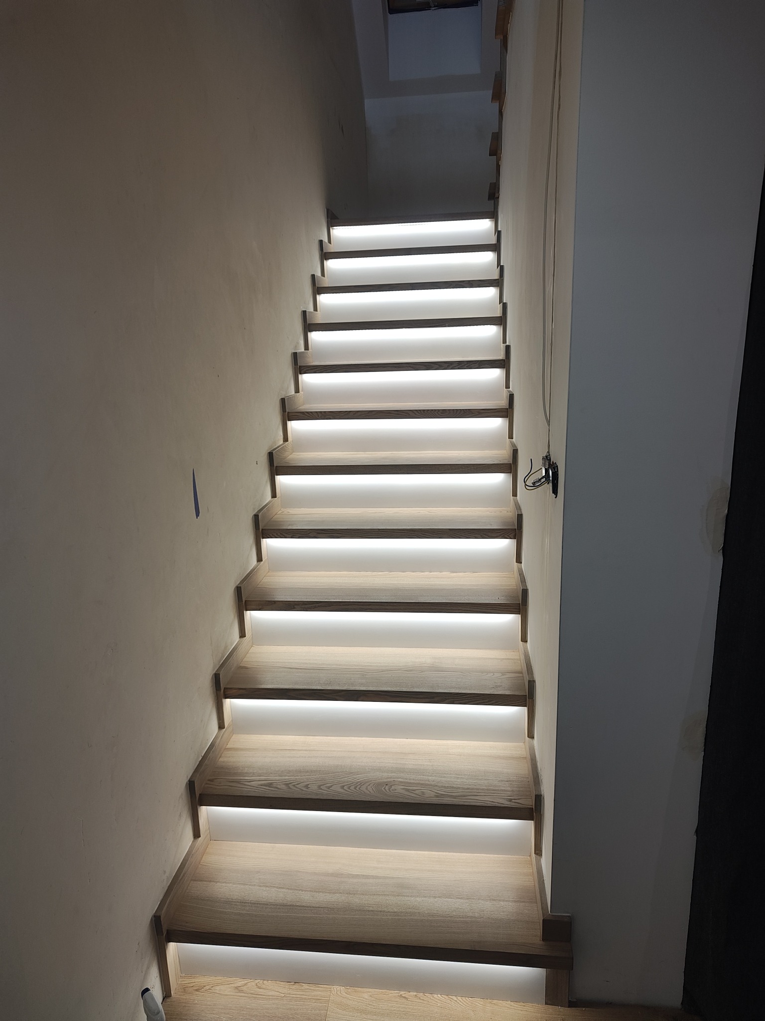 Nowoczesne schody drewniane z subtelnym oświetleniem LED, prowadzące w górę. Widoczne detale wykończenia i minimalistyczny design.