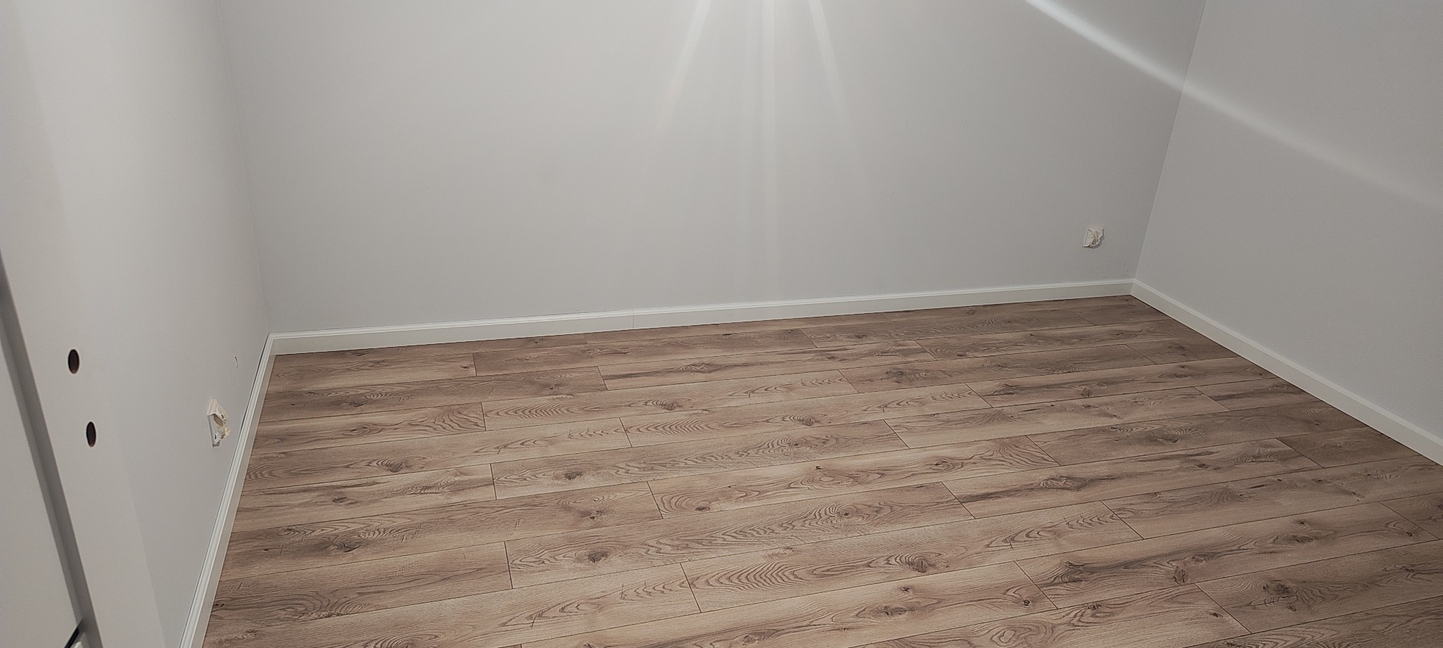 Ułożone panele podłogowe w pokoju z białymi ścianami i listwami przypodłogowymi. Realizacja w Dobroszyce. Widoczne gniazdka elektryczne.