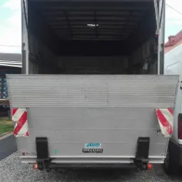 Otwarta przestrzeń ładunkowa busa transportowego z rampą załadowczą, widok z tyłu na żwirowe podłoże.