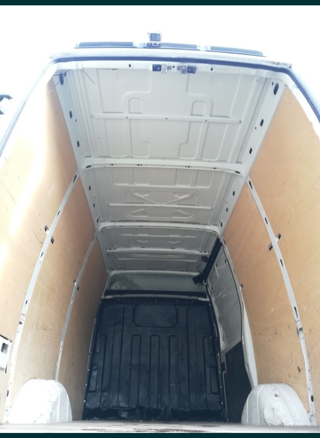 Wnętrze furgonetki wyłożone płytami OSB, widok z tyłu na puste miejsce ładunkowe, czarna gumowa podłoga.