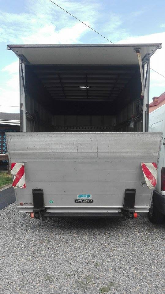 Otwarta przestrzeń ładunkowa busa transportowego z rampą załadowczą, widok z tyłu na żwirowe podłoże.