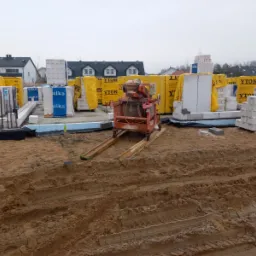 Przygotowanie do budowy fundamentów: widoczny wykop, bloczki fundamentowe Silka i Ytong na paletach, oraz betoniarka na placu budowy.