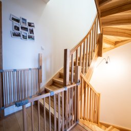 EASY BUILDERS SPÓŁKA Z OGRANICZONĄ ODPOWIEDZIALNOŚCIĄ - Drewniane schody kręcone z barierką zabezpieczającą dla dzieci, na ścianie galeria zdjęć, jasne wnętrze.