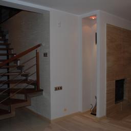 Firma Budowlana Styl-Bud - Nowoczesne wnętrze z drewnianymi schodami z metalową balustradą, ścianą pokrytą dekoracyjną fakturą i obudowanym kominkiem z jasnego kamienia.