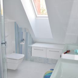 Firma Budowlana Styl-Bud - Jasna łazienka na poddaszu z oknem dachowym, białą ceramiką, umywalkami z przezroczystego szkła i niebieskimi akcentami na płytkach i tekstyliach.